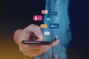 Un cellulare tra le mani di una persona con delle icone che fluttuano sopra di lui