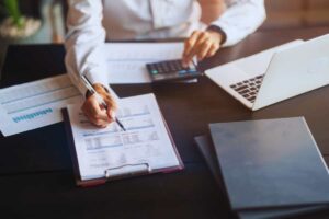 Persona seduta ad una scrivania che scrive su un foglio con intorno altre pratiche